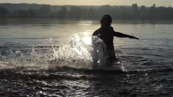 Homem feliz faz salpicos em um lago ao pôr do sol em slo-mo — Vídeo de Stock