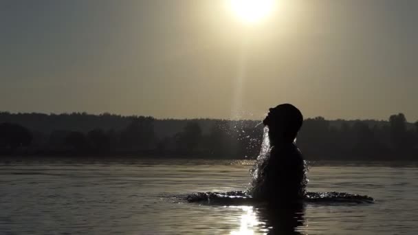 Jonge man springt uit een bos meer bij zonsondergang in slo-mo — Stockvideo