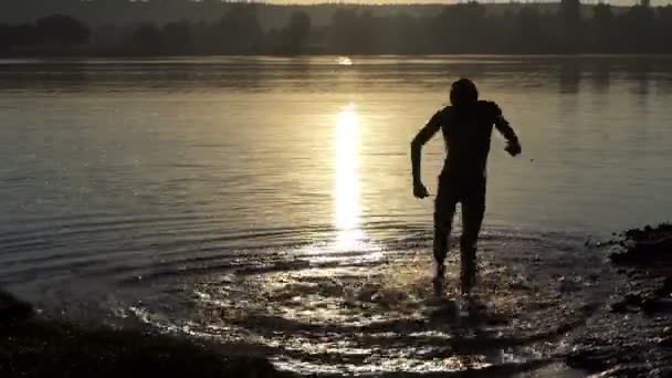 Felice giovane uomo balla in un lago al tramonto — Video Stock