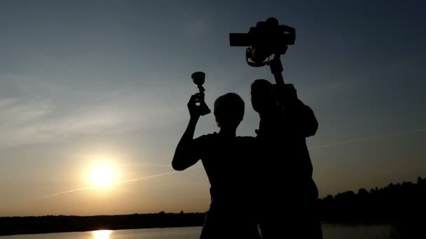 Twee jonge mannen houden van een stedicam en een kampioen kom bij zonsondergang — Stockvideo