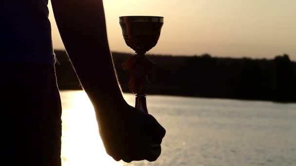 Mão do homem mantém uma tigela vencedora em um banco do lago ao pôr do sol — Vídeo de Stock