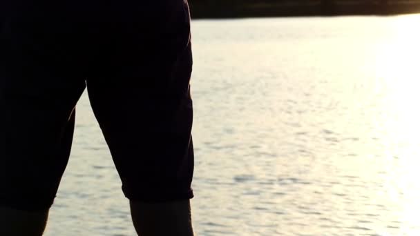 Muž snižuje jeho šampion misku na jezero při západu slunce v slo-mo — Stock video