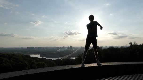 Energisk man dansar rumba på floden bank vägg vid solnedgången i slo-mo — Stockvideo
