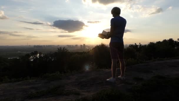 Estudante inteligente fica e olha através de um livro ao pôr do sol em slo-mo — Vídeo de Stock