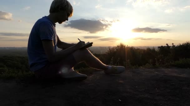 Akıllı bir adam bir peri masalı bir çimenlikte slo-mo gün batımında yazıyor — Stok video