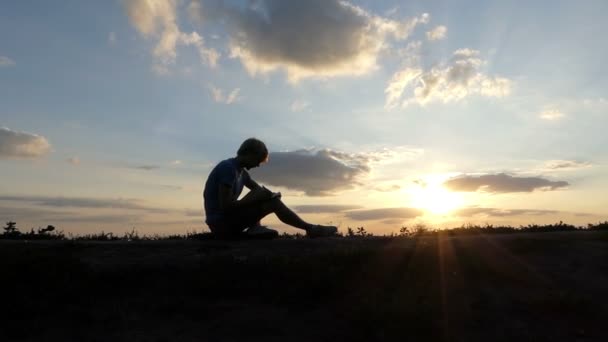 Giovane uomo scrive un articolo su un prato al tramonto a Slo-mo — Video Stock