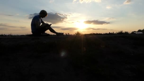 Junge Bloggerin schreibt einen Artikel auf einem Rasen bei Sonnenuntergang in slo-mo — Stockvideo