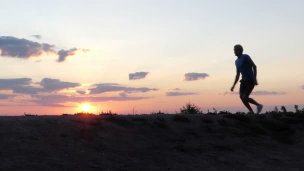 Щасливий чоловік біжить і стрибає на галявині на заході сонця в шлю-мо — стокове відео