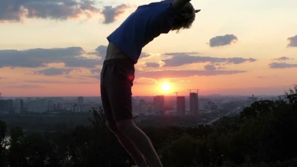 Sportive man raises hands and spans his back at sunset in slo-mo — Stock Video