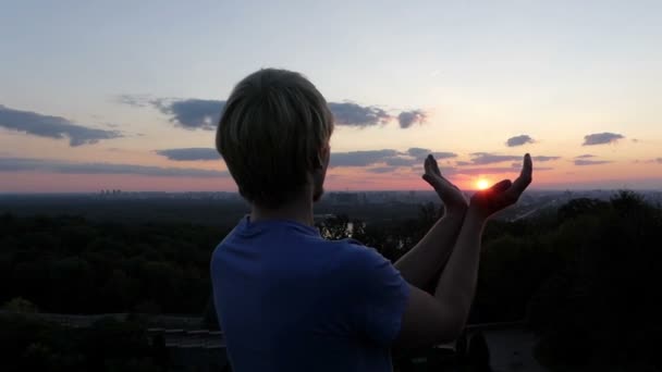 Jonge man houdt zon in zijn handen bij zonsondergang in Kiev in slo-mo — Stockvideo