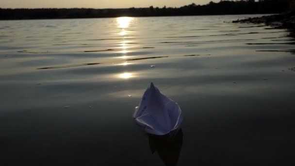 Un barco de papel blanco flota en el agua de un lago al atardecer en slo-mo — Vídeo de stock