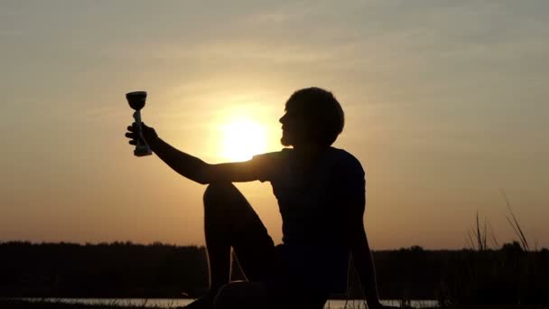 Young man sits on a lake bank and kisses his champion bowl in slo-mo — Stock Video