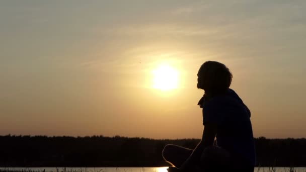 Young man sits on a lake bank and raises his champion bowl in slo-mo — Stock Video