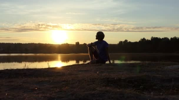 Романтик пьет чай сидя на берегу озера на закате в сло-мо — стоковое видео