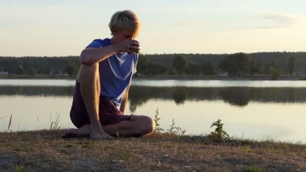 Kreativer Mann trinkt Kaffee am Seeufer bei Sonnenuntergang im Slo-mo — Stockvideo