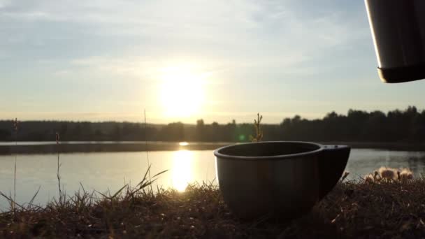 El té caliente se vierte de un frasco en una taza en una orilla del lago en slo-mo — Vídeo de stock