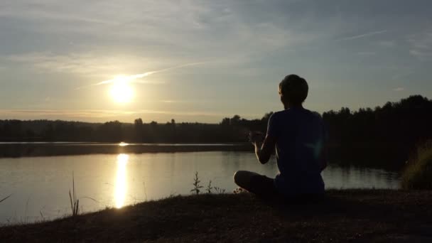 Iluminado hombre bebe té en una orilla del lago al atardecer en slo-mo — Vídeo de stock