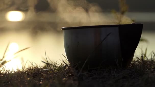 Taza metálica de té se coloca en una orilla del lago al atardecer en slo-mo — Vídeos de Stock