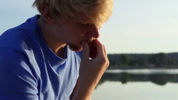 Молодой студент читает учебник на берегу озера в сло-мо — стоковое видео