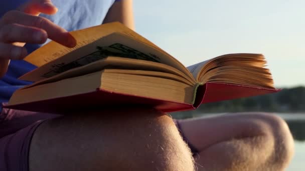 Mladý student čte beletrii na břehu jezera v slo-mo — Stock video