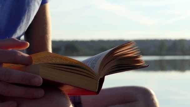 Um estudante lê um livro de ficção num banco de lago em Slo-mo — Vídeo de Stock