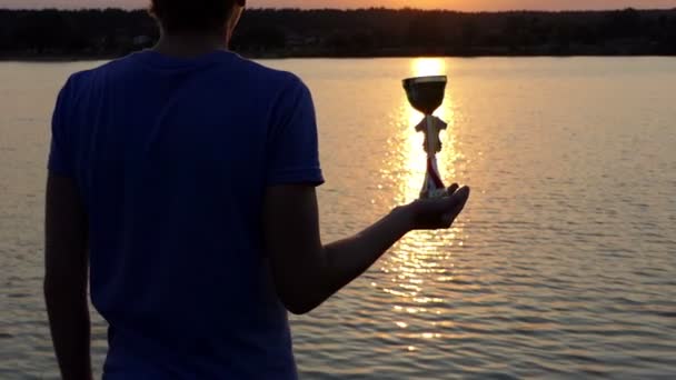 Young man keeps his winner bowl on a sunpath at a lake — Stock Video