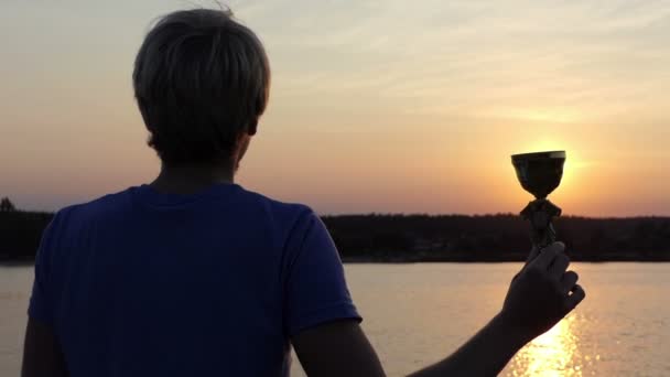 Glücklicher Mann hält seine Siegerschale auf einem Sonnenweg am See — Stockvideo