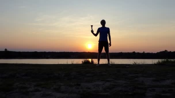 Молодой чемпион поднимает свой кубок победителя на берегу озера в сло-мо — стоковое видео