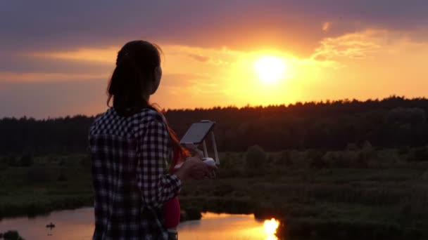 Smal kvinna hanterar en panel för att styra en drönare i solnedgången — Stockvideo
