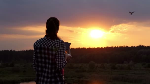 Νεαρή γυναίκα λειτουργεί ένα πάνελ για τον έλεγχο ενός quadracopter στο ηλιοβασίλεμα — Αρχείο Βίντεο