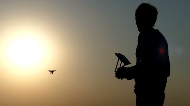 Eine Nahaufnahme eines Mannes, eines Kontrollpanels und einer fliegenden Drohne bei Sonnenuntergang — Stockvideo