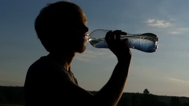 Блондинка п'є воду з пластикової пляшки на заході сонця в шлю-мо — стокове відео