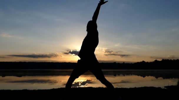Homem loiro dança disco em um banco do lago ao pôr-do-sol em slo-mo — Vídeo de Stock