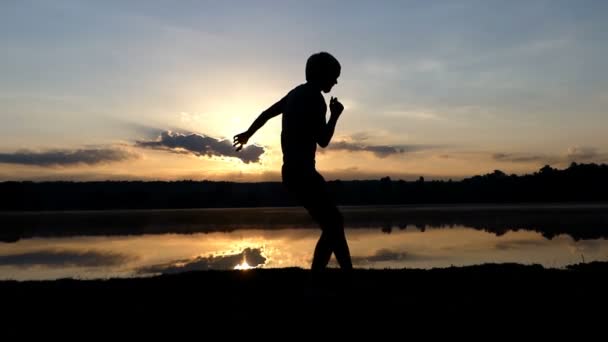 Hombre alegre baila danza estilo en una orilla del lago al atardecer — Vídeo de stock