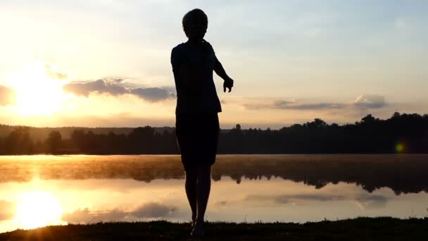Homem alegre dança rave em um banco de lago ao pôr do sol — Vídeo de Stock