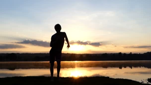 Hombre feliz baila estilo libre en una orilla del lago al atardecer en slo-mo — Vídeos de Stock