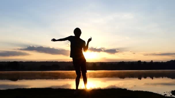 Hombre enérgico baila discoteca en una orilla del lago al atardecer en slo-mo — Vídeo de stock