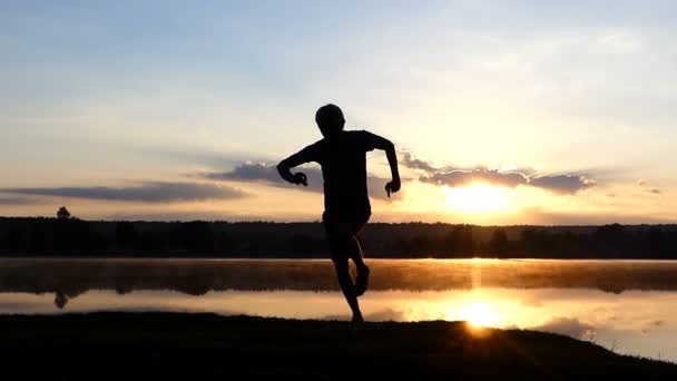 Homem alegre dança discoteca em um banco de lago ao pôr do sol em slo-mo — Vídeo de Stock