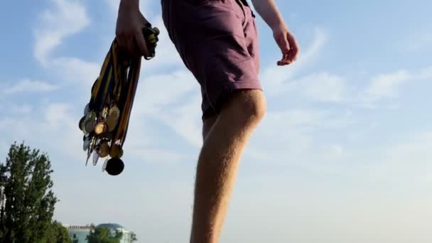 Las piernas masculinas van con un montón de medallas en un carril en verano — Vídeo de stock