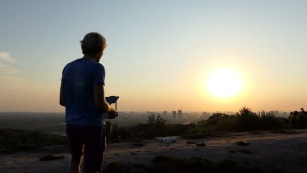 El hombre brillante controla un cuadracóptero nuevo al atardecer en slo-mo — Vídeo de stock