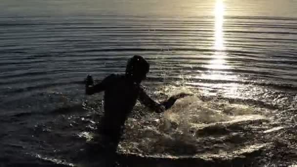 Νεαρός άνδρας χτυπάει το νερό της λίμνης για να διασκεδάσει στο ηλιοβασίλεμα σε slo-mo — Αρχείο Βίντεο