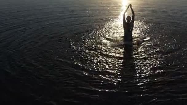 Jovem faz salpicos levantando água do lago ao pôr do sol em slo-mo — Vídeo de Stock