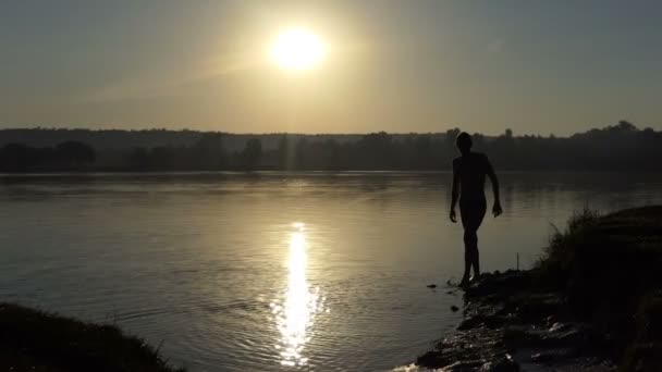 Feliz hombre hace salpicaduras corriendo en un lago al atardecer en slo-mo — Vídeo de stock