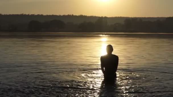 陽気な男は、スローモーションで夕暮れ時に湖に立って水しぶき — ストック動画