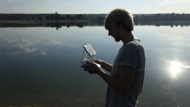 Hi-tech человек смотрит на свою панель и управляет дроном на озере в slo-mo — стоковое видео
