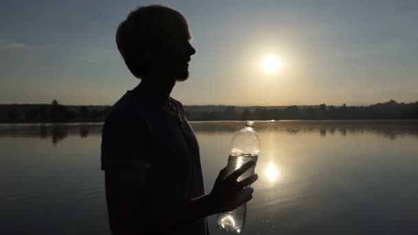 Homem elegante levanta uma garrafa de plástico para beber água ao pôr do sol em slo-mo — Vídeo de Stock