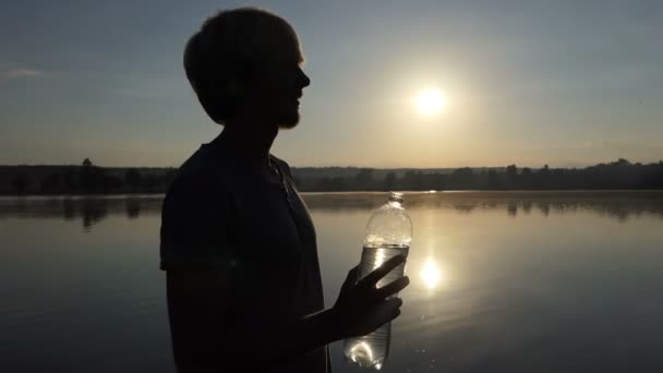 Stijlvolle man liften een plastic fles om te drinken van water bij zonsondergang in slo-mo — Stockvideo