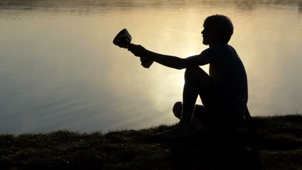 Orgulloso hombre se sienta en una orilla del lago y mira a un recipiente ganador — Vídeos de Stock