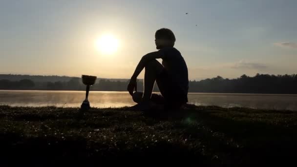 Un uomo allegro siede su una riva del lago. Una ciotola vincente è qui vicino a Slo-mo — Video Stock