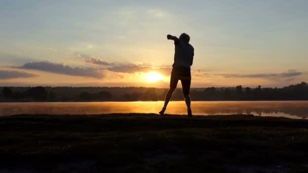 Jeune homme danse style libre sur une rive du lac au coucher du soleil — Video